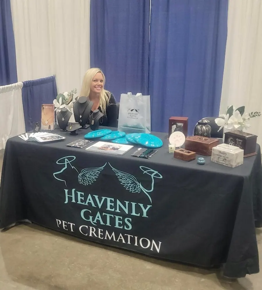 A Heavenly Gates team member at an event booth, with urns and keepsakes displayed on the table.