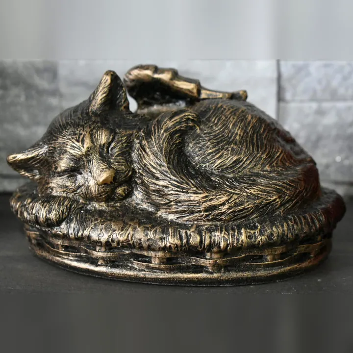 A bronze urn shaped like a sleeping cat with angel wings, curled on a cushion.