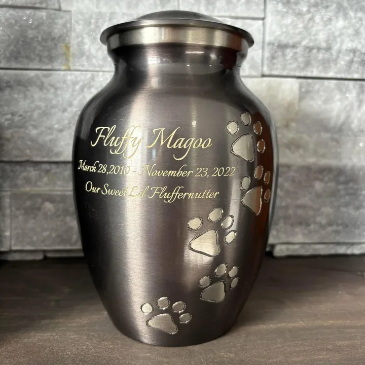 A dark brass urn engraved with a name and dates, with paw prints climbing the side.