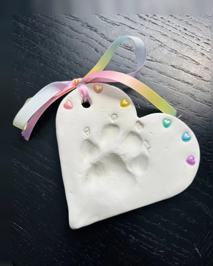 A heart-shaped clay paw print with small pastel hearts along its edge, tied with a rainbow ribbon.