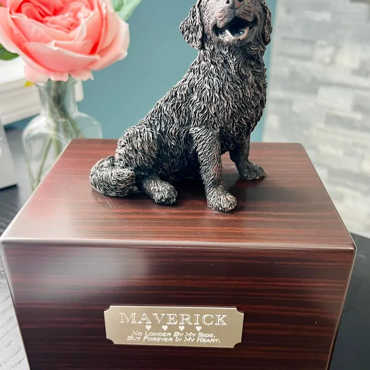 A wood-grain urn box with a bronze dog figurine on top and an engraved name plate.