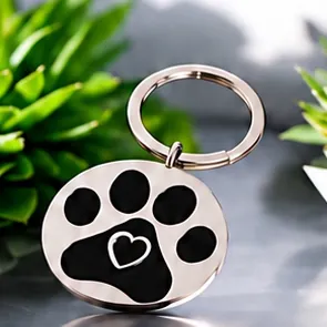 A round silver keychain with a black paw print and a heart cut-out.